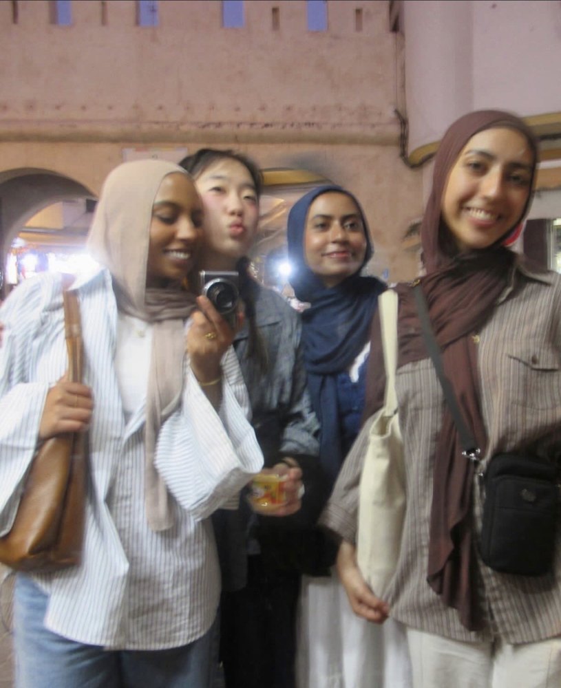 Four friends smiling together at night in front of a pink wall in Morocco