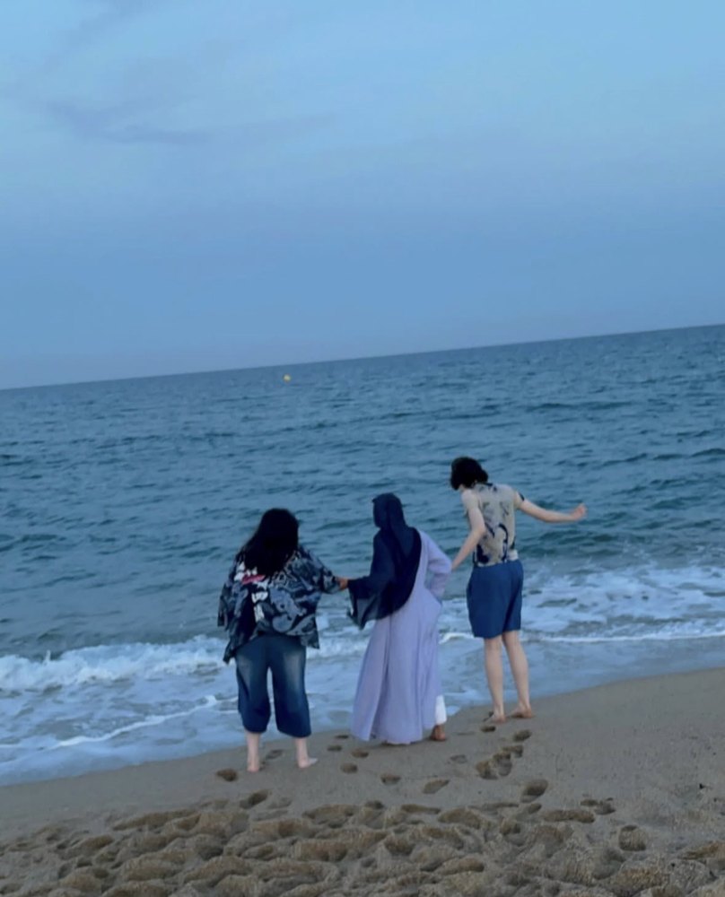 Three people holding hands at the edge of the sea on a Barcelona beach at dusk