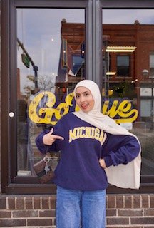 Nadia in a Michigan sweatshirt pointing at a yellow sign in front of a storefront in Ann Arbor