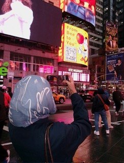 A person in a hooded jacket taking a photo of the bright billboards in Times Square