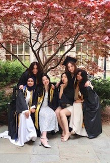 Nadia and friends in graduation gowns posing under a red-leafed tree
