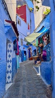 A narrow blue-painted street in Chefchaouen with hanging scarves and a green awning